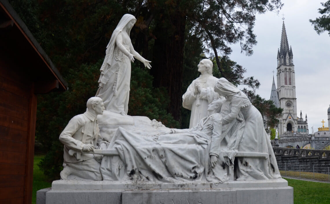 Estatua de enfermo en cama recibiendo la unción